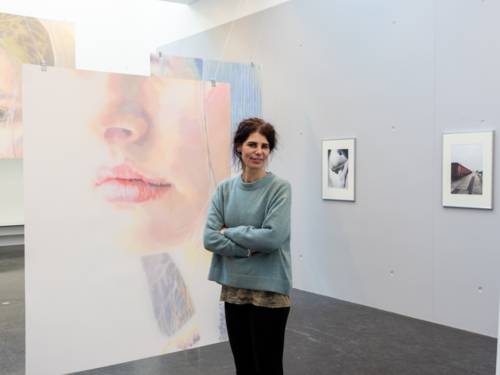 Zu sehen ist die Künstlerin Hanna Nitsch vor ihren großformatigen Arbeiten, die sanfte Malerei von angeschnittenen Gesichtern.