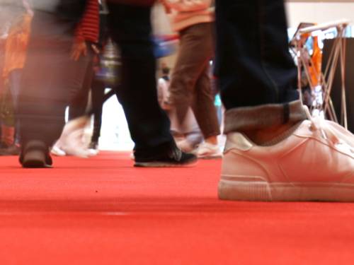 Blick aus der Froschperspektive auf die Schuhe von Menschen, die über einen roten Teppich gehen.