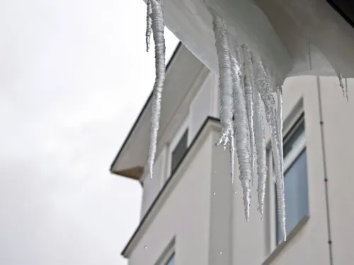 Eiszapfen hängen vor einem Fenster und tauen langsam.