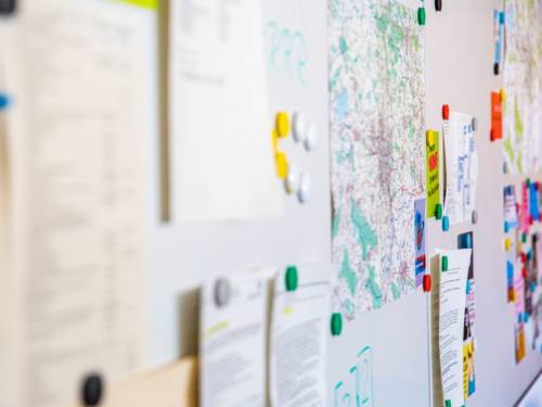 An einer weißen Magnetwand sind verschiedene Infos befestigt, darunter Karten und Flyer.