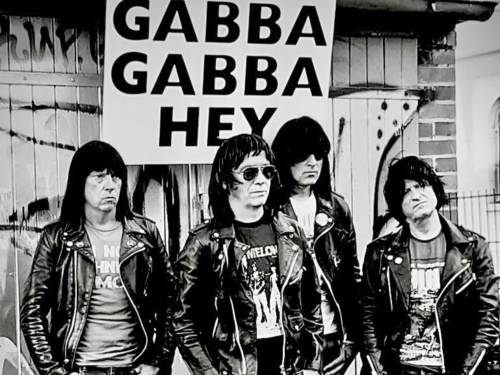 Schwarzweißaufnahme vierer Männer in Lederjacken vor einem Schild mit der Aufschrift "Gabba Gabba Hey".