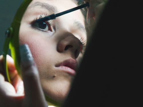 Ein Mädchen tuscht sich die Wimpern. Man sieht sie nur im Spiegel