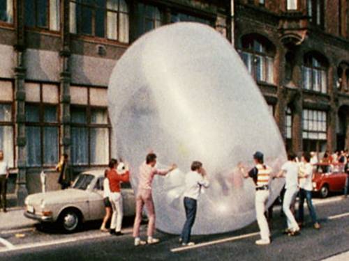 Mehrere Personen rollen einen riesigen Gummiball eine Straße entlang