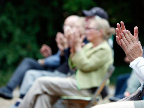 Eine Gruppe älterer Menschen sitzt draußen und klatscht mit den Händen.