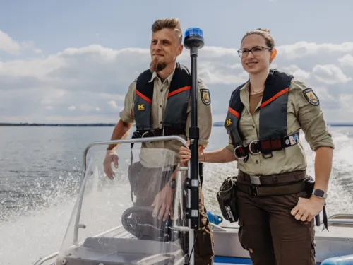Eine Rangerin und ein Ranger fahren mit einem Boot.