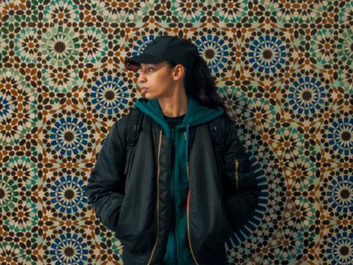 Eine junge Frau steht an einer bunten Wand - sie guckt zur Seite