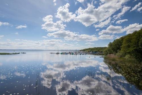 Blick über einen See, in dem sich Wolken spiegeln, im Hintergrund ein Steg mit Booten