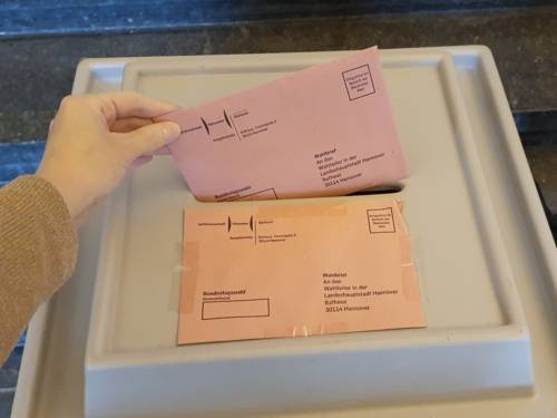 Ausschnitt einer Hand, die einen Wahlbrief in eine Wahlurne wirft