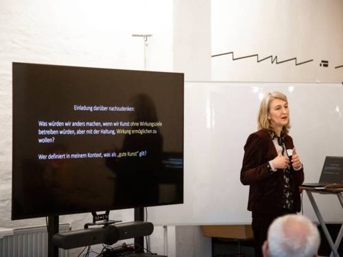 Ein Frau vor einem Bildschirm hält eine Rede.