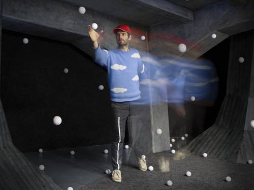 Ein Mann in einem schwarzen Raum mit vielen liegenden und fliegenden kleinen weißen Bällen