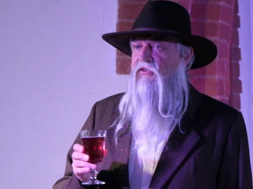 Mann mit weißem Bart, Hut und einem Glas Rotwein in der Hand.
