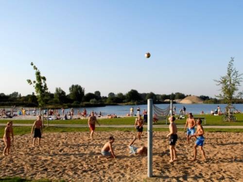 vorne Beachvolleyball spielende Jugendliche, eine Liegewiese, im Hintergrund der See