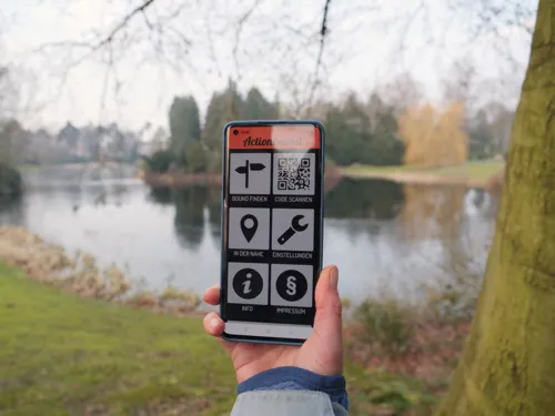 Eine Hand, die mit einem Handy im Gr&uuml;nen unterwegs ist.