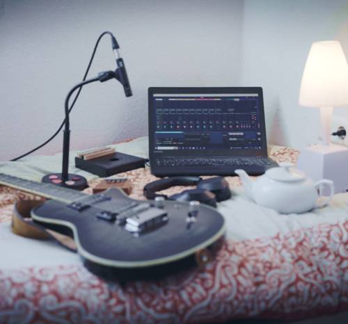 Ein Bett mit unter Anderem einer Gitarre, Mikrofon, Kopfhörern und einem Laptop darauf.