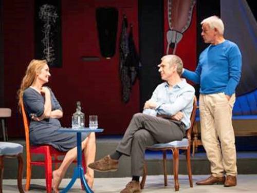 Eine Frau und ein Mann sitzen an einem Tisch, rechts davon steht ein dritter Mann.