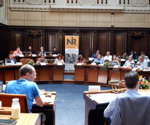 Die im Kreis aufgestellten Tische im Hodlersaal sind gut besetzt. In der Bildmitte ein Banner mit dem Logo des Niedersächsischen Integrationsrates (NIR).
