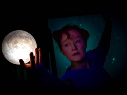 Theaterszene: Eine Frau schaut auf ihre Hand und den Mond in ihrer Hand.