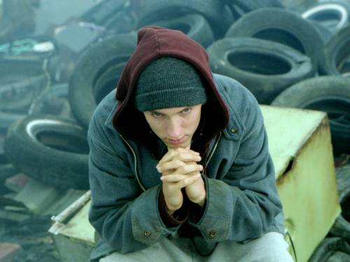 Ein Mann sitzt auf einer Kiste. Hinter ihm sind viele Autoreifen und anderer Abfall zu sehen.