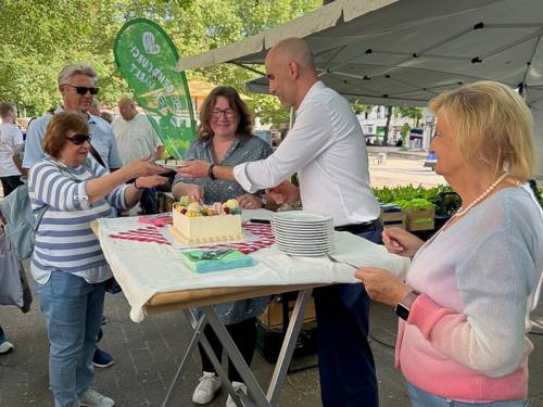 Mehrere Personen um einen Stand, an dem Torte angeschnitten wird.