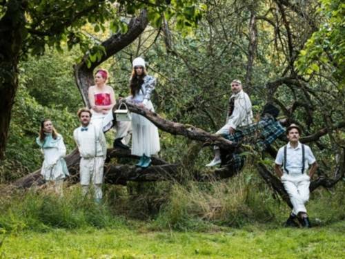 Drei Männer und drei Frauen in Theaterkostümen in einer Grünanlage