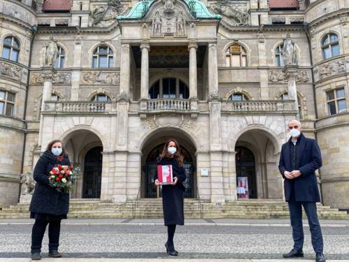 Drei Personen vor dem Neuen Rathaus Hannover. Sie tragen einen Mund-Nasen-Schutz und halten Abstand.