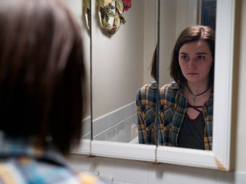 Autumn - ein siebzehnjähriges Mädchen - steht vor einem Spiegel und schaut sich traurig an.