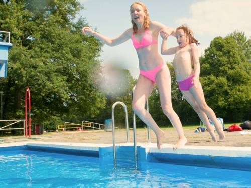Eine Frau und ein Kind springen in einem Freibad vom Beckenrand ins Wasser.