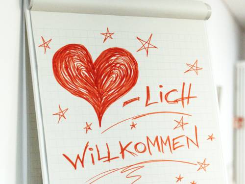 Auf einem Flipchart ist ein Herz gemalt, dazu steht: "-lich willkommen"