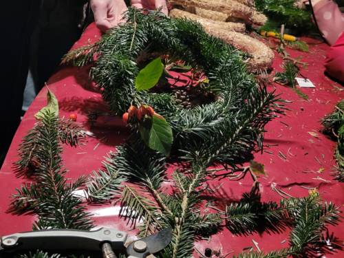 Tannenzweige, Gartenschere und ein fast fertig gebundener Adventkranz auf einem Tisch