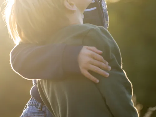 Im Gegenlicht der Sonne legt ein Junge einem anderen einen Arm um die Schulter.
