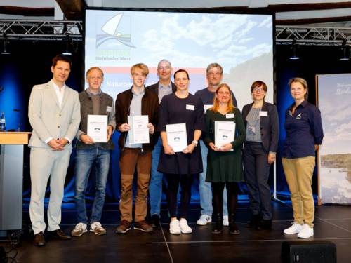Neun Personen stehen auf einer Bühne, dabei werden vier Urkunden gehalten.