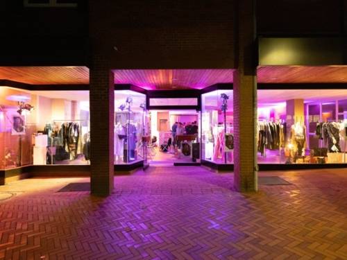 Eine Schaufensterzeile bei Nacht in lila Neonlicht. Im Ladengeschäft sind hauptsächlich Kleidungsstücke zu sehen.
