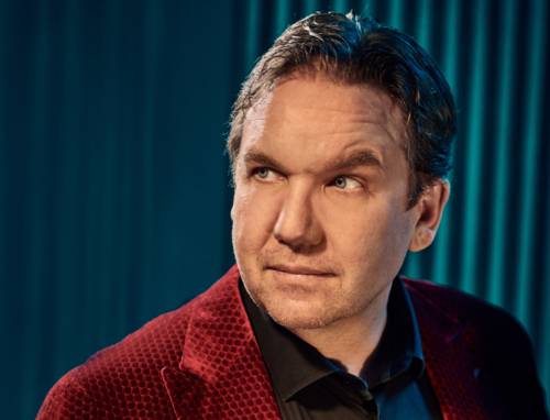 Nahporträt eines leicht zur Seite schauenden Mannes mit kurzem Haar und Dreitagebart in Hemd und Jackett