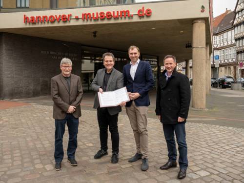 Vier Männer stehen vor einem Gebäude mit der Aufschrift hannover-museum.de