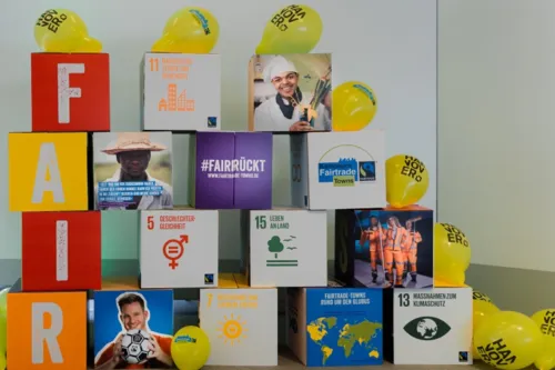 Pappwürfel mit Fotos und Symbolen der SDGs und den Buchstaben "Fair". Drumherum Luftballons mit dem Hannover-Logo.