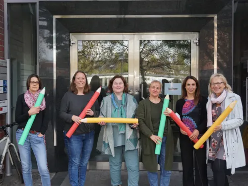 Personen, mit überdimensionierten Buntstiften, in einem Hauseingang