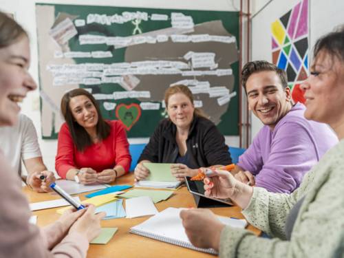 Personen sitzen an einem Tisch und beschriften Moderationskärtchen.