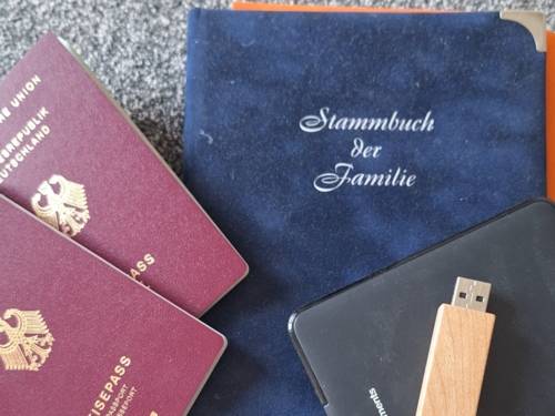 zwei Reisepässe liegen schräg über einem Familienstammbuch und darüber liegt eine Festplatte und ein USB Stick