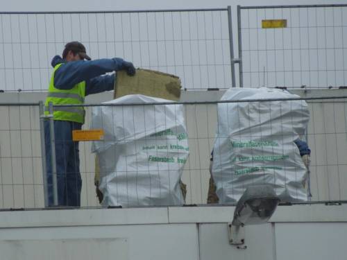 Arbeiter, der Abfälle aus künstlichen Mineralfasern in speziellen Abfallsäcken mit Warnaufschrift entsorgt