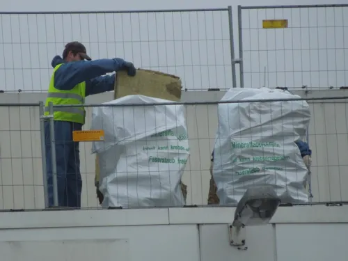 Arbeiter, der Abf&auml;lle aus k&uuml;nstlichen Mineralfasern in speziellen Abfalls&auml;cken mit Warnaufschrift entsorgt