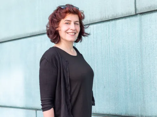 Porträtfoto einer Frau vor einer türkisfarbenen Fassade.