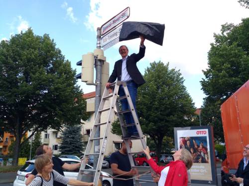 Ein Mann auf einer Leiter enthüllt ein neues Straßenschild mit der Aufschrift "Ada-Lessing-Straße"
