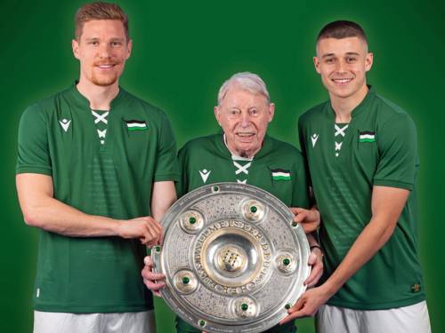 Zwei junge und ein alter Mann mit der Meisterschale in grünen Trikots.