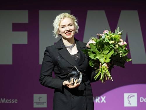 Eine Frau mit Blumenstrauß und Preis aus Kristall.