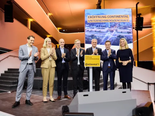 Menschengruppe im Foyer eines modernen Gebäudes vor Plakat mit der Aufschrift "Eröffnung Continental Unternehmenszentrale"
