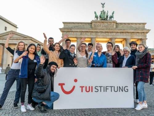 Sechzehn junge Menschen mit einem Plakat mit der Schrift TUI Stiftung vor dem Brandenburger Tor