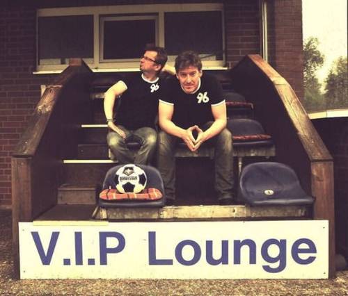 Zwei Männer in Hannover-96-Shirts sitzen auf einer Treppe vor einem Haus, im Vordergrund ein Schild mit der Schrift V.I.P. Lounge