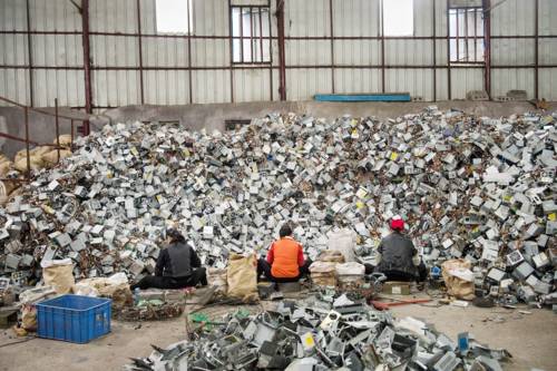 Drei Menschen sitzen vor einer großen Menge Elektroschrott, den sie bearbeiten.