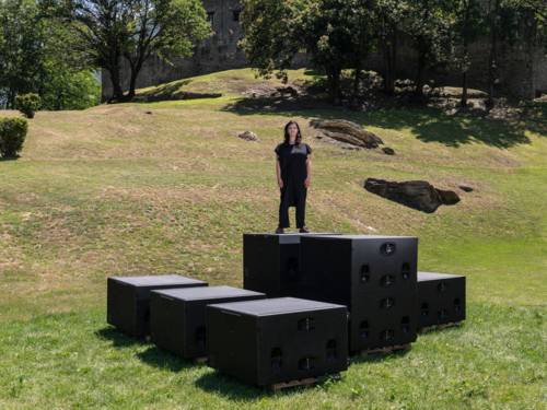 Ein Frau steht vor auf einer grünen Wiese, vor ihr liegen große Lautsprecher im Gras.
