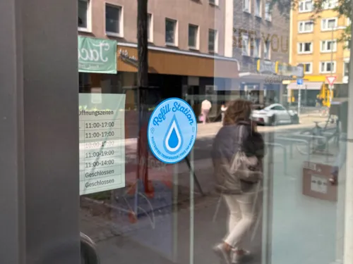 Ein Aufkleber mit einem blauen Tropfen darauf. Er klebt an einer Scheibe.